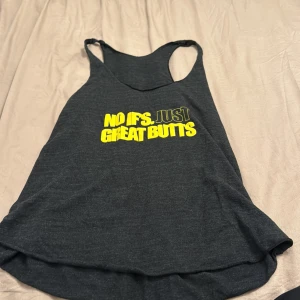 Mörkgrå linnetopp med text - En mörkgrå linnetopp med texten 'NO IF'S. JUST GREAT BUTTS' i gult och vitt på framsidan. Toppen har en lös passform och är ärmlös.