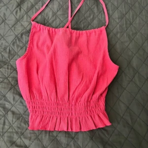 Rosa linnetopp från Gina Tricot - En oanvänd rosa linnetopp från Gina Tricot med smala axelband och rynkad nederkant. Toppen har en lös passform och är tillverkad i ett lätt och luftigt material. 