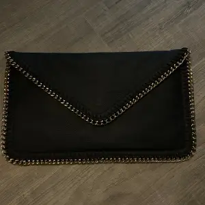 En svart väska, funkar att ha som en kuvertväska men finns även kedje band till. Använd fåtal gånger 