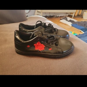 Svarta sneakers röd ros - Svarta sneakers med broderad röd ros. Köpta som storlek 39 men upplevdes som små i storlek (passade ej mig), lägger dem därför som storlek38. Ej mycket använda.
