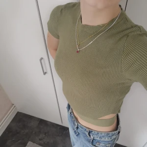 Croppad topp - En supersnygg croppad topp i en olivgrön färg. Den är ribbad och har supersnygga hål vid sidorna. Från Bershka i storlek S, men tight i modellen. Som ny. 