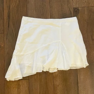 Stradivarius- vit minikjol med volang - En vit minikjol med volang och dragkedja i sidan. Huvudmaterial: 100% bomull. Originalpris: 329kr, men köpt på rea för 196kr. Varan är i nyskick och provad en gång, men var för stor. 