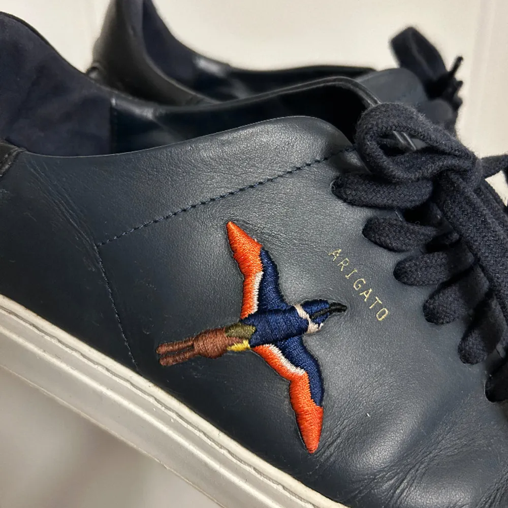 Ett par Arigato Clean 90 Sneaker Navy Leather som är använda vid fåtal tillfällen. Ordinarie pris: 2500kr. Skor.