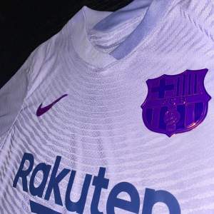 En mycket fin FC Barcelona 2021/22 borta tröja. Tröjan är i mycket bra skick, använd ett fåtal gånger. Inget fel alls med den. Tröjan är player version, storlek M. Hör av er vid frågor! :)