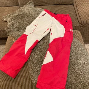 Skidbyxor från Picture i toppskick - stlk 14/164 - Superfin skidbyxa i cool design med skönt tunnare invändigt fleecefoder. Mörkare cerise. 4 fickor, reglerbara i midjan, ventilation insida lår, knappar vid benslut + snölås. Picture är ett franskt märke som startades av tre vänner 2008 med miljöfokus