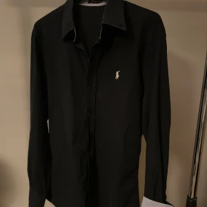 Ralph lauren skjorta  - Tjena, säljer nu en svart Ralph Lauren skjorta med mörkblå ton i strl M, men passar S. Armar och krage är ljusblå, vit randig på insidan vilket ger en snygg detalj om man gillar uppvikta ärmar. Skjortan är i väldigt bra skick och vårt pris 329kr