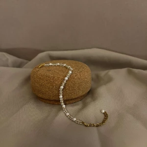 Armband- Vera - Vårt armband Vera är vårt minsta armband och består av små vita pärlor och små beiga pärlor. Låset och kedjan är guldpläterade. Namn: Vera Längd: Hela 21 cm Pärlor 14,5 