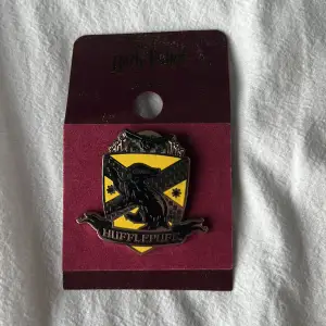 En officiell Harry Potter pin av elevhemmet Hufflepuff. Själva paketeringen har blivit böjd med det har inte påverkat produkten