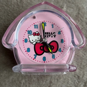 Väckarklocka Hello Kitty - Söt väckarklocka med Hello Kitty-motiv, drivs av ett AA-batteri. En flik på baksidan har lossnat, se bild, men inget som påverkas och det syns inte framifrån. 