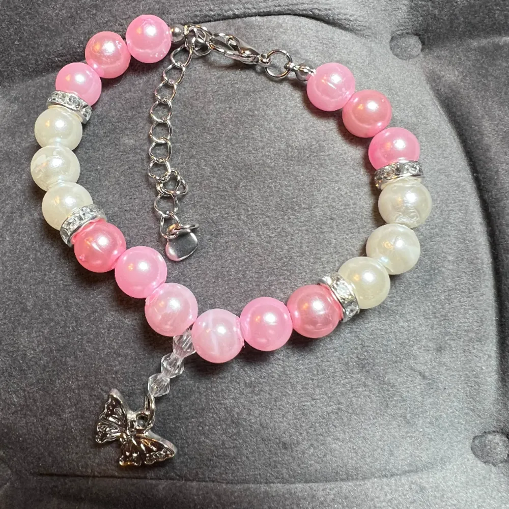 Pärlarmband med vita och rosa pärlor, glittriga mellanplattor och silvrig fjäril och spänne. Justerbar passform mellan 16-21 cm.. Accessoarer.