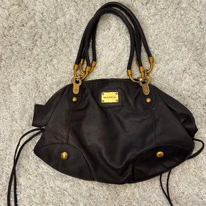 Väska - Mörkbrun Väska med gulddetaljer från dolce&gabbana. Fint skick utan defekter. Vill du köpa trycker du på köp nu, jag postar inom 24h