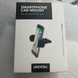 Mobilhållare - En mobilhållare till bilens fläktgaller. Kartongen har gått sönder lite när jag öppnade varan men den har aldrig använts så varan är i nyskick.