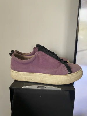 Lilla sneakers  - Lila mocka sneakers med svarta volanger på framsidan. Skinn på insidan. Ganska andvända. Kom gärna med prisförslag. 