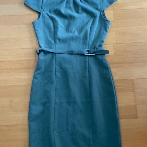 Grön fodralklänning storlek S/36, H&M - Figursydd fodralklänning med skärp. Fint skick. Når till knäna på mig som är 1.68 lång. 