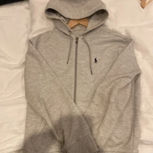 Grå Ralph Lauren Hoodie - Säljer denna klassiska ralph lauren hoodien till ett rimligt pris, tröjan har lite smutsfläckar som man kan skrubba bort (inte orkar fixa själv då den inte används av mig)