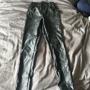 Svarta skinnbyxor - Ett par svarta skinnbyxor i storlek xs. Byxorna har en tight passform och är tillverkade av syntetiskt material som imiterar skinn.