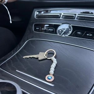 Nyckelring med pärlor och hängsmycke - En elegant handgjord nyckelring med vita pärlor och ett hängsmycke i form av ett öga. Nyckelringen har en metallring för att fästa nycklar.