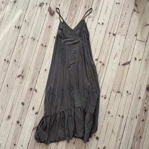 Grå klänning från Tiger of Sweden - En elegant gråbrun klänning från Tiger of Sweden med tunna axelband och ett subtilt mönster. Klänningen har en volangdetalj vid fållen och en v-ringad halslinje. passar nog mer en M än L