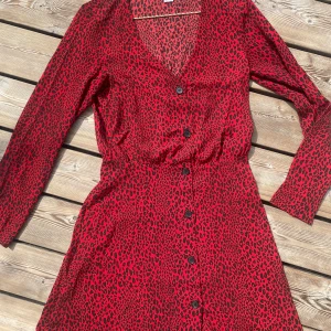 Röd klänning 38 - H&m röd klänning, storlek 38 En röd klänning med leopardmönster och knappar framtill. Klänningen har långa ärmar och en V-ringning. Tunn och luftig 