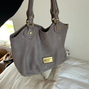 Marc Jacobs väska  - Jätte fin Marc Jacobs väska i en grå-beige-rosa färg!  Bra skick! Finns även ett långt band. Rymlig, man får plats med dator etc.  Mått: ca 40x30 cm Priset går att diskutera. 