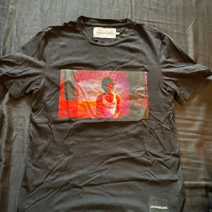 Calvin Klein t-shirt - En CK t-shirt med häftigt motiv. Storleken står XS men passar mig som bör M så någonstans mellan S/M är nog korrekta storleken. Vid frågor eller bilder så hör av er!