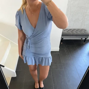 Klänning - Blå klänning med puffärmar och volanger från Ginatrico i storlek M. Väldigt fint skick.