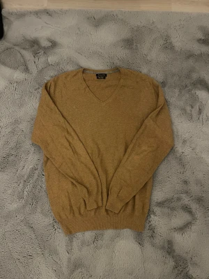 Stickad cashmere tröja från Massimo Dutti  - Säljer en beige/brun stickad tröja från Massimo Dutti i storlek M. Tröjan har v-ringad hals och långa ärmar, perfekt för dig som gillar enkel och stilren design. Materialet är cashmere och cotton och den ribbade kanten vid ärmslut och nederkant ger en snygg passform.