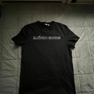 Svart Björn Borg t-shirt i bomull - Svart t-shirt från Björn Borg i mjuk bomull. Klassisk passform med rund hals och korta ärmar. Stor vit logga framtill. Helt oanvänd har haft den i ungefär en vecka men den var förstor så säljer den nu.