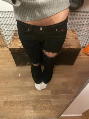 Svarta lågmidjade bootcut jeans med slitningar - Svarta jeans från Levi's med bootcut passform och snygga slitningar vid knäna. Modellen har klassisk femficksdesign, knapp och dragkedja framtill samt låg midja. Jeansen är tillverkade i jeansmaterial och har en cool, edgy vibe. Innerbenslöngd 78cm, rakt över midja 36cm