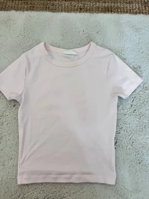 Ljusrosa  t-shirt  - En enkel och fräsch ljusrosa t-shirt med rund hals och korta ärmar. 