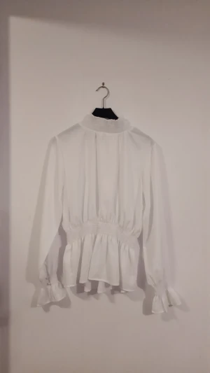 En vit långärmad blus med luftigt tyg och med en halskrage. (Vuxenstorlek) - Den är oanvänd och fläckfri. Storlek 38. Pris 80 kr +FRAKT