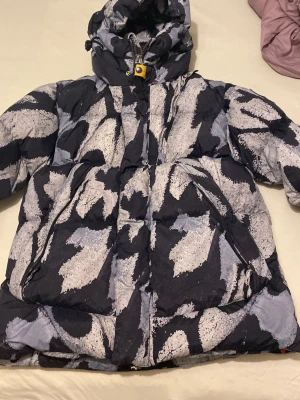 Parajumpers Outback pufferjacka M - Säljer en Parajumpers Outback pufferjacka i storlek M med unikt abstrakt mönster i svart och grått. Jackan har huva med snörning, dragkedja och tryckknappar framtill samt patch på ärmen. Perfekt för dig som vill sticka ut med en cool vinterjacka.