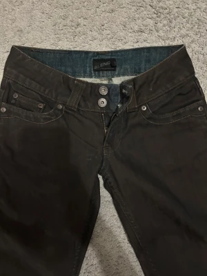 Svarta jeans från Blend, straight fit - Säljer ett par brun svarta jeans från Blend med klassisk femficksdesign och snygga kontrastsömmar. Modellen har rak/utsvängd passform, låg midja och detaljerade bakfickor med broderade sömmar. Jeansen är tillverkade i bomull och har dragkedja och dubbla knappar framtill.