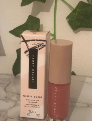 Fenty Beauty Gloss Bomb Lipgloss - Fenty Beauty Gloss Bomb Universal Lip Luminizer i en snygg rosa nyans. Kommer i en stilren förpackning med beige lock och transparent tub. Ger glansiga, fylliga läppar med en mjuk känsla. Perfekt för att boosta din look med extra shine.
