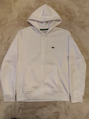 LACOSTE Tröja med dragkedja  - En vit Lacoste tröja med en dragkedja med rikt och äkta matrial. Vill du diskutera pris skriv