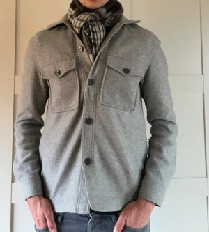 Grå overshirt från Studio Total - Snygg grå overshirt från Studio Total i storlek S men passar M. Jackan har två stora bröstfickor med knappar, klassisk krage och knäppning framtill. Nypris 950kr.