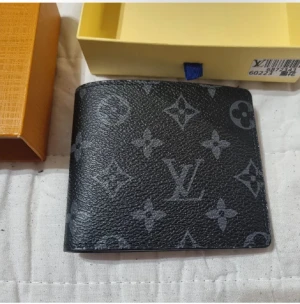  plånbok - Snygg svart plånbok med klassiskt monogrammönster i grått. Tillverkad i tåligt skinn och ikoniska blommor över hela ytan. Perfekt storlek för fickan och stilren design som sticker ut.