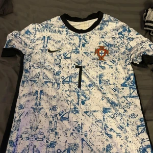 Portugal Ronaldo fotbollströja Nike S - Portugal fotbollströja från Nike med Ronaldo 7 på ryggen. Tröjan har ett unikt blåvitt mönster, svart krage och är tillverkad i Dri-Fit material. Perfekt för dig som älskar fotboll och vill bära landslagets färger.