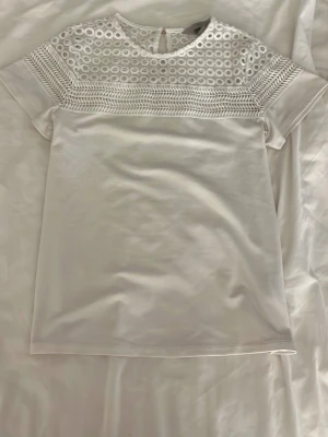 Vit blus med spets från H&M XS - Säljer en vit blus från H&M i storlek XS. Toppen har korta ärmar. Överdelen är dekorerad med broderad spets.