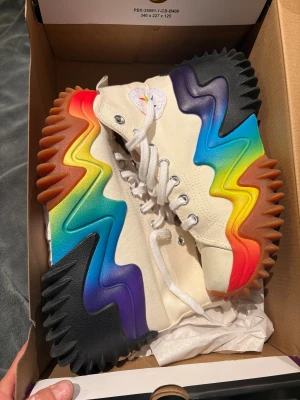 Converse Run Star Motion Pride sneakers stl.37,5 nya i kartong - Unika Converse Run Star Motion sneakers i canvas med högt skaft och chunky sula i regnbågsfärger. Skorna har vit ovandel, snörning, regnbågsdetaljer på plösen och Converse-logga med regnbågsstjärna. Sulan är vågig och färgglad med svart, lila, blå, grön, gul, orange och röd. Nya i kartong( innermått23 cm)