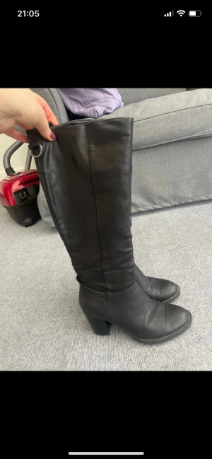 Svarta stövlar med klack i skinn - Säljer ett par svarta stövlar i skinn med rund tå och stabil klack. Stövlarna har en snygg metallring och snörningsdetalj upptill. Perfekt till höst och vinter för dig som gillar klassisk stil med lite edge.