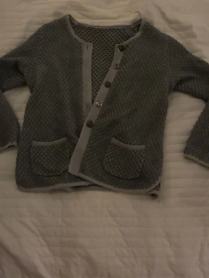 Grå stickad kofta med fickor - Säljer en grå stickad kofta med snyggt diskret mönster och ribbade kanter. Koftan har knappar framtill och två praktiska fickor. Perfekt för chill dagar. Passar dig som gillar lite unik stil.
