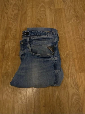 Replay ljusblå jeans slim fit - Säljer ett par ljusblå jeans från Replay med klassisk femficksdesign och snygga slitningar. Jeansen har slim fit-passning och raka ben, med Replay-logga på bakfickan och läderpatch i midjan. Perfekt för dig som gillar en avslappnad men stilren look.