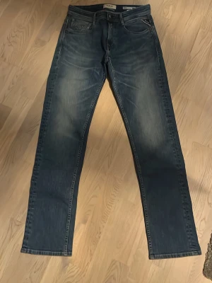 Replay blå jeans straight fit - Säljer ett par snygga blå jeans från Replay med klassisk femficksdesign och raka ben. Jeansen har en cool tvättad look med ljusare partier och tydliga sömmar. Passar dig som gillar en enkel och stilren jeansstil. Märke syns tydligt på bakfickan.