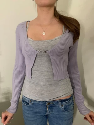 Ljuslila croppad kofta💟 - Superfin ljuslila croppad kofta med ribbad struktur och lång ärm. Koftan har ett snyggt metallspänne framtill som stängning och är gjord i stickat material. Perfekt att styla över ett linne eller t-shirt för en söt look. Skriv vid frågor! 💜