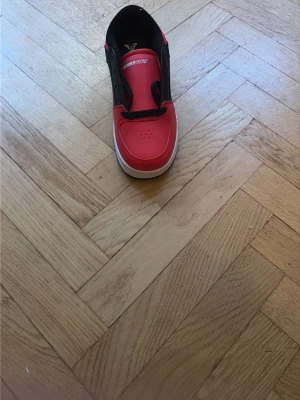 Röd och svart barn Heelys sneaker med hjul - Coola Heelys sneakers i rött och svart med vita detaljer och hjul under sulan. Skon har rund tå, platt sula och snörning. Perfekt för dig som vill glida fram på hjul och sticka ut med en färgstark stil. Materialet är syntet och skon har X-logga på sidan.