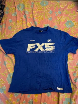 En blå t-shirt med lite skrivning på den. - Den har knappst blivit använt. Inga fläckar, inga revor och inga tecken på användning syns på t-skjortan. Obs! Oroa dig inte, jag stryker den förstås innan leverans.