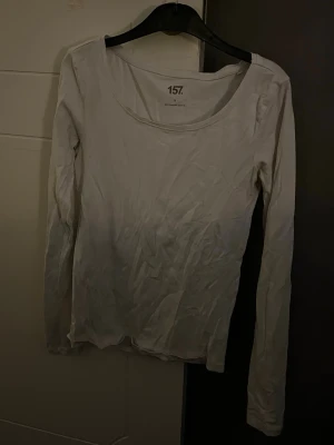 Vit långärmad topp från 157 - Säljer en enkel vit långärmad topp från 157 med rund halsringning. Toppen är i mjuk bomull och har en normal passform som funkar till många olika stilar. Perfekt att ha som basplagg eller att styla med andra plagg.