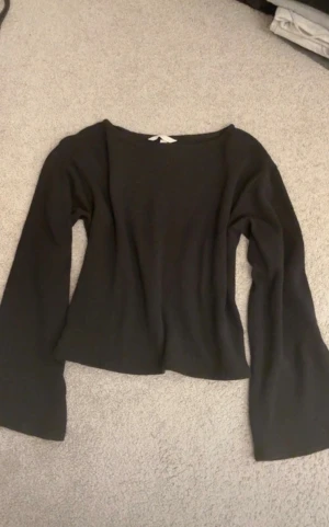 Svart långärmad topp med utsvängda ärmar - Säljer en svart stickad långärmad topp med utsvängda ärmar och rund halsringning. Toppen har en enkel och stilren design, är croppad i modellen och är tillverkad i ett mjukt stickat material som känns skönt mot huden.