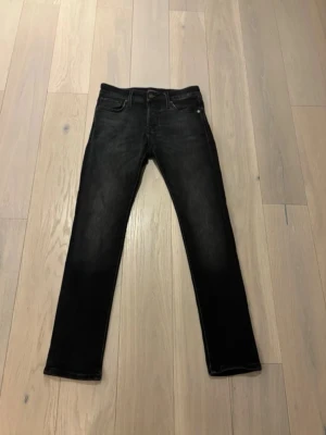 Svarta jeans från Jack & Jones - Säljer ett par svarta jeans från Jack & Jones med klassisk femficksdesign och diskret tvättad look. Jeansen har rak passform och normal midja, tillverkade i mjukt bomullsmaterial med lite stretch för extra komfort. Perfekt för dig som gillar stilrena och enkla jeans.  W27 L30